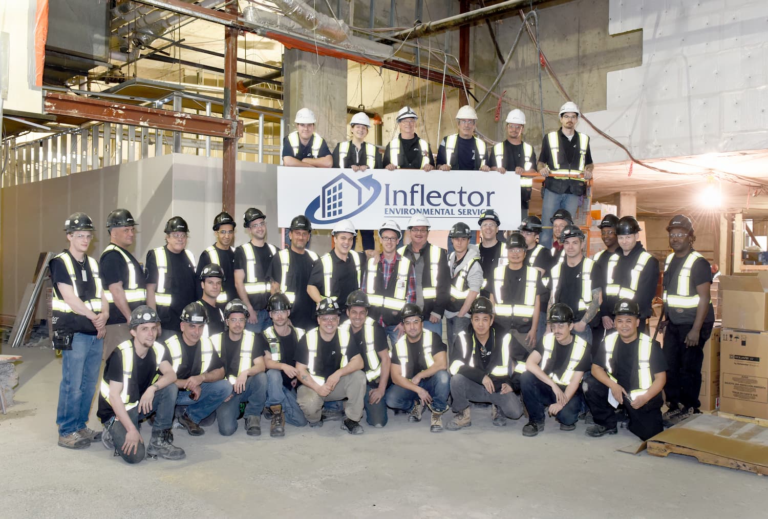 Large group of workers wearing safety vests and helmets with Inflector banner
