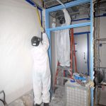 Worker taking asbestos material off a wall